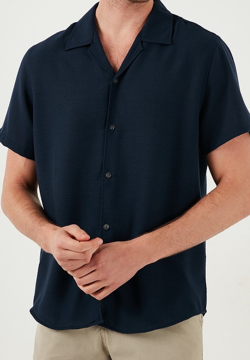 Ciemnogranatowa koszula na krótki rękaw z kołnierzykiem typu point, wykonana z lekkiego materiału, o luźnym kroju i subtelnym połysku.