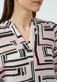 Bluzka z długim rękawem i kołnierzykiem, z geometrycznym wzorem w kolorach czarnym, różowym i białym, wykonana z teksturowanej tkaniny, z częściowym zapięciem na guziki.