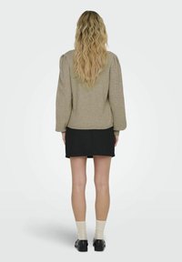 Beige texturerad tröja med puffärmar, i kombination med en svart kjol, vita strumpor och svarta skor. Bakifrån syns flödande hår.