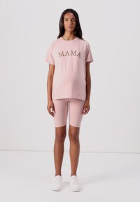 Pink cotton t-shirt with the word "MAMA" in bold brown letters, paired with matching pink biker shorts and white sneakers.