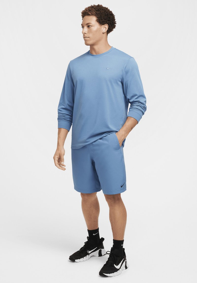 Jasnoniebieska koszula z długim rękawem i dopasowane szorty z logo Nike. Czarne buty sportowe z teksturowaną podeszwą i wsparciem kostki.