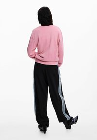 Rožinė palaidinė su laisvu siluetu ir ribotais rankogaliais, derinama su juodomis kelnėmis su šviesiai mėlynomis šoninėmis juostomis. Matomos juodos aukštakulnės batai.