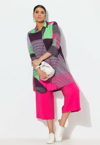 Tunic a blocchi di colore in viola, verde e rosa con strisce orizzontali; abbinata a culottes fucsia e sneakers bianche. Borsa a mano.