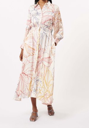 Femme portant une robe à fleurs à manches longues boutonnée avec des motifs linéaires multicolores, associée à des sandales argentées à talons avec brides.