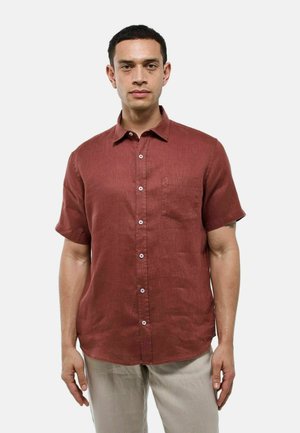 Chemise à manches courtes de couleur rouille en tissu texturé avec une fermeture boutonnée à l'avant et une poche poitrine. Des boutons de couleur claire contrastent avec la chemise.
