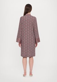 Mauve Kleid mit einem Diamantmuster in Hellgrün und Schwarz, mit langen Ärmeln, hohem Kragen und geradem Schnitt, das bis zur Mitte der Wade fällt.