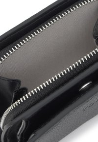 Cartera de cuero negro con textura, cremallera plateada abierta que muestra el interior de tela gris claro y múltiples compartimentos.