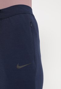 Pantalons de sport bleu marine en tissu doux, avec une poche zippée et un logo Nike gris foncé sur la cuisse gauche.