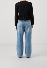 Haut péplum noir à manches longues associé à un jean large bleu clair, avec poches arrière et texture en denim délavé.