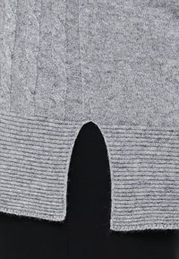 Grå strikket genser med kabelstrikkedesign, ribbede kanter og splittet helm. Myk tekstur med et subtilt melert mønster.
