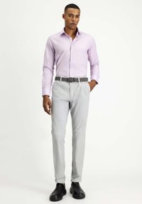 Camisa de color púrpura claro, pantalones grises y zapatos negros. El conjunto presenta un diseño ajustado con una textura suave y un cinturón trenzado.