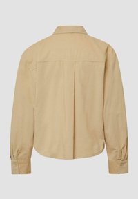 Camicia beige con maniche lunghe e polsini abbottonati, una piega al centro della schiena e colletto diritto, vista da dietro su uno sfondo semplice.