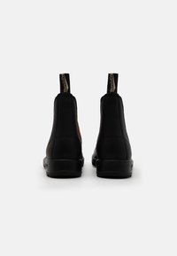 Stivaletti neri alla caviglia con pannelli laterali elasticizzati, tomaia texture, anelli per il tiraggio e suola in gomma piatta. Presentano un design minimalista e una costruzione robusta.