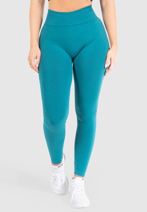 Teal legging met een hoge tailleband, gemaakt van rekbaar materiaal. Gladde textuur met een aansluitend ontwerp, gecombineerd met witte sportschoenen.