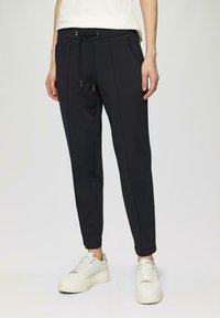 Zwarte joggerbroek met een koord in de taille, tapered pijpen en zijzakken. Draag met witte platform sneakers.