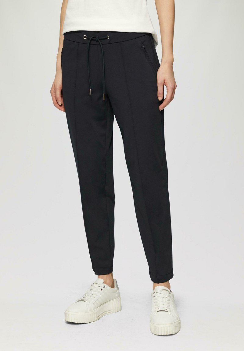 Zwarte joggerbroek met een koord in de taille, tapered pijpen en zijzakken. Draag met witte platform sneakers.