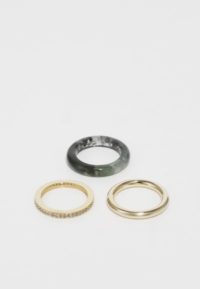 Tri prstene na bielom povrchu: jeden tmavý mramorovaný prsteň, jeden zlatý prsteň s malými kameňmi a jeden jednoduchý zlatý prsteň.