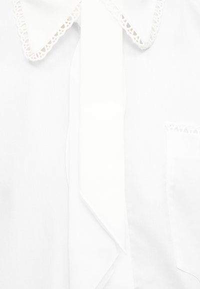 Blouse blanche avec un col pointu bordé de dentelle et une longue fine cravate en tissu à l'avant, comportant une poche ornée de dentelle.