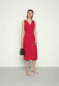 Vestido fúcsia até ao joelho com decote em V, sem mangas e detalhes plissados. Acompanhado de sandálias nuas de tiras e uma pequena bolsa preta.
