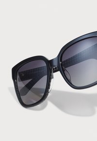 Ochelari de soare negri, supradimensionați, cu lentile degradate și imprimeu houndstooth pe interiorul bratelor. Fabricati din plastic neted, având un finisaj lucios.