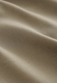 Țesătură de culoare bej deschis, cu o textură netedă și o ușoară strălucire; drapată în cute fine, evidențiind un țesut uniform și delicat.
