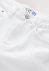 Biele široké rifle s vysokým pásom a denimu, s gombíkovým zapínaním, pútkami na opasok a kontrastným šitím. Na vnútornej strane pásu je viditeľná značka.