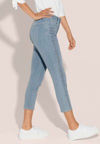 Helle blaue, taillierte Jeans mit seitlicher Verzierung, schmaler Schnitt und Gesäßtaschen. Kombiniert mit weißen Sneakers. Glatte Denim-Oberfläche.