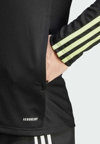 Zwarte sportshirt heeft een gemêleerde stof, zijzak en groene strepenaccenten op de mouwen. Aeroready-merk zichtbaar.