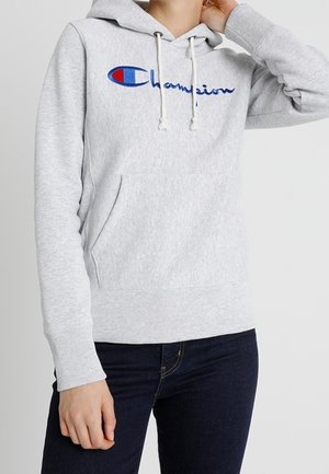 Grå fleecehuva med en känguruficka, justerbara snörningar och broderad blå och röd "Champion"-logotyp på framsidan.