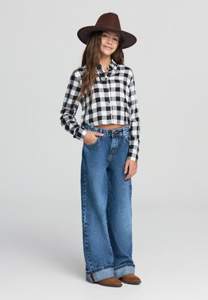 Camicia in flanella a quadri bianco e nero, jeans a gamba larga in denim blu, cappello marrone, calzature marrone scuro, design casual con motivi distintivi.