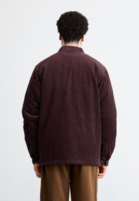 Mørke lilla kordfløjljakke med krave, knapmanchetter og en loose fit. Stoffet har lodrette ribber og en glat tekstur.