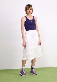 Marineblå tanktopp, hvit midiskjørt med volangkant, lilla sneakers og rutete sokker. Enkel design med en myk stofftekstur.