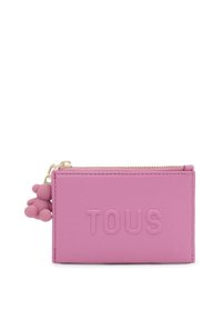 Różowy skórzany portfel z wytłoczonym logo "TOUS", zamknięciem na suwak oraz zabawnym breloczkiem w kształcie misia przymocowanym do zamka. Gładka faktura.