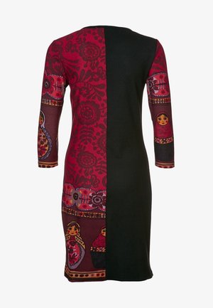 Kleid, bei dem eine Hälfte einfarbig schwarz ist und die andere Hälfte rote Blumenmuster sowie Motive russischer Matrjoschka-Puppen auf Ärmeln und Rock zeigt.