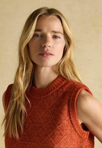 Kootud ilma varrukateta sviiter erksas oranžis värvis, millel on tekstureeritud teemantimuster ja ribaga ümar kaelus.