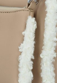 Beige leren handtas met een witte donzige textuur langs de randen, ritssluiting en metalen hardware accenten. Gladde oppervlakte met gedetailleerde stiksels.