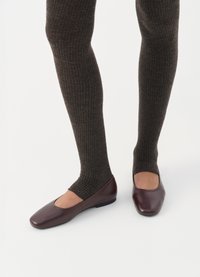 Leggings marroni a coste abbinati a ballerine in pelle bordeaux con punta quadrata e tacco basso, che mostrano una trama liscia.