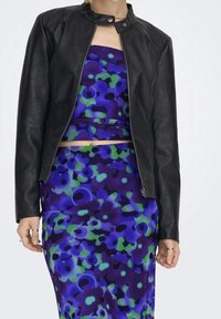 Giacca moto in pelle nera con colletto arrotondato e dettagli sui lati delle spalle, abbinata a un vestito con fantasia floreale vibrante blu e verde.