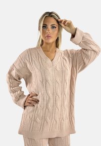 Lichtroze kabelgebreide trui met lange mouwen, een V-hals en geribbelde manchetten. De textuur is dik en knus, met een losse pasvorm.