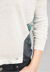 Maglione leggero a maglia con una parte superiore color crema e una parte inferiore a motivo teal e grigio scuro; dettaglio dei bottoni argentati sull'orlo.