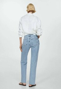 Jeans de tiro alto de color azul claro con un corte recto, que cuentan con dos bolsillos traseros. Combinados con una camisa de lino blanca de botones.