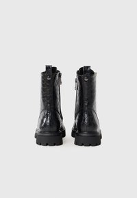 Bottines noires en cuir verni texturé avec un motif hexagonal, dotées d'une fermeture éclair latérale et de semelles en caoutchouc chunky.