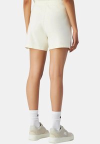 Crème-kleurige shorts van katoen, met een relaxte fit en een elastische tailleband, gecombineerd met grijze sneakers en witte sokken.