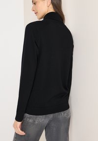 Černý svetr s měkkou pletenou texturou, vybavený límcem a dlouhými rukávy. Kombinován se šedými džíny, zdůrazňujícími pohodlný střih.
