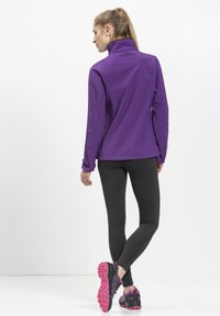 Lilla langærmet træningsjakke med høj krave, parret med sorte leggins og sorte/lyserøde træningssko. Glat stof, tætsiddende design.