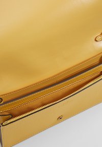 Intérieur de sac à main en cuir jaune avec une texture lisse et un compartiment zippé doté d'une fermeture éclair dorée et d'une doublure.