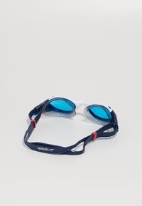 Speedo simglasögon med blå linser, vit ram och mörkblå rem med röda detaljer; texturerad tätning för komfort och passform.