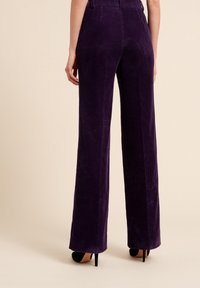 Lila kordflorsbyxor med vida ben, vertikala ränder, hög midja och en mjuk textur, i kombination med svarta klackar. Bakifrån.