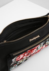 Czarna skórzana torba z wyszywanym kwiatowym wzorem w kolorach czerwonym, różowym i niebieskim. Posiada złoty zamek błyskawiczny oraz logo na przedniej stronie. Wewnątrz znajduje się kilka przegródek.