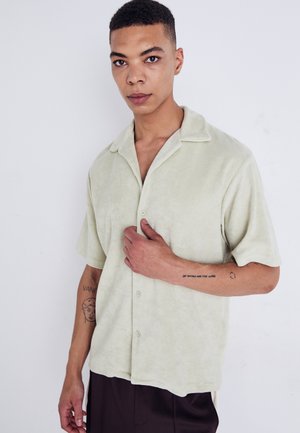 Chemise vert clair à manches courtes, en tissu doux, avec une fermeture à boutons et un col pointu ; texture subtile et design décontracté.